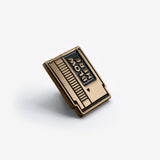 A black and gold soft enamel pin in a retro game cartridge look with the text 'blow here' sitting at an angle on a light grey background.